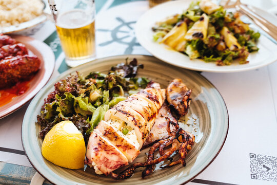 Gegrillter Kalmar (Calamari, Kalamari, Tintenfisch) mit Salat und Zitrone am Teller