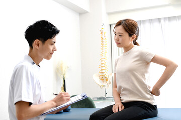 白衣の男性とカウンセリングをうける腰を抑えるアジア人女性