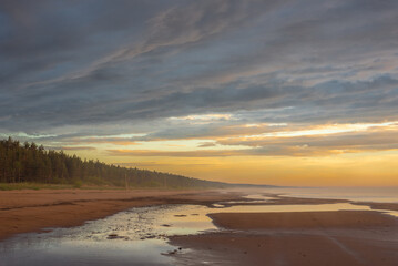 Empty sandy beach of Baltic sea covered with fog after rain during the sunset at summer