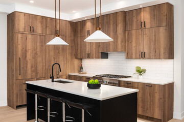 A kitchen detail with wood cabinets, a black faucet, subway tile backsplash, and gold light...