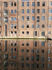 Facade of an old warehouse built of red bricks mirroring in the water of a canal in Hamburg, Germany