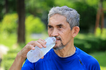 Senior Asian man is drinking water after morning exercise in the park for rehydration of sweat loss...
