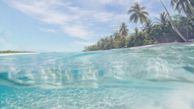 Half underwater slow motion of clear turquoise sea water. Idyllic vacations in the resort at the tropical white sand beach with palm trees