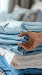 Fototapeta premium Closeup of womans hand holding a stack of clean blue and white bed sheets on sunny day