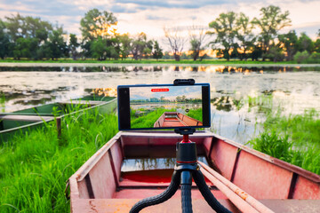 Smartphone mounted on a tripod taking a video of beautiful sunrise on the shore of the river