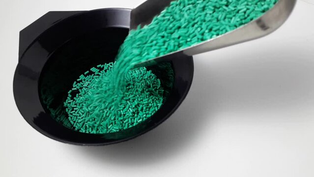 Turquoise masterbatch granules are poured into a black measuring cup.Color pigment carrier polymer in the plastics industry