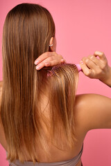 Woman brushing wet hair with pink background, maintaining long hair for hair health and grooming