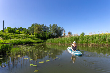 Fototapeta premium Suzdal, Russia, Golden Ring: A tourist girl swims along the river past the sights of the ancient Russian city of Suzdal in the warm summer