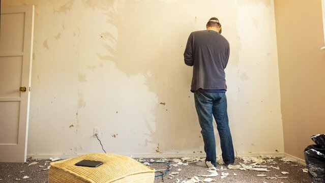 A worker uses a clothing steamer to take off wallpaper in an apartment.