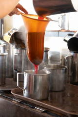 Making Thai iced tea with a tea bag in a strainer over a glass with ice cubes.