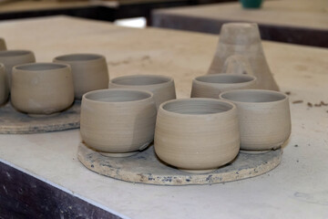 A pottery class. There are several unfinished clay cups on a rotating platform.