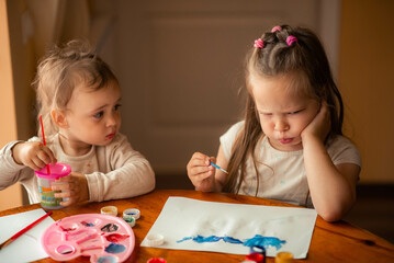 Fototapeta premium two sisters paint with paints, one is 1 year old and the older one is 5 years old.