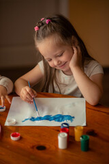 5 year old girl draws with paints. she has long hair and light colored clothes