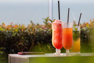 Three drinks with straws in them are on a table. One is a watermelon juice, one is a mix fruit drink, and one is a yellow drink