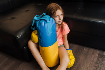Happy girl, Ukrainian athlete boxer child sitting indoors wearing boxing gloves with a yellow and...