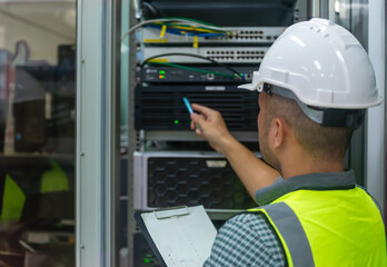 an asian man IT technician working on network Internet cables and servers and try to checklist on the paper board to maintenance the data sharing network