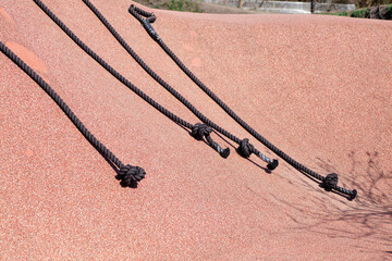 Climbing ropes with handles on a playground structure in bright sunlight.