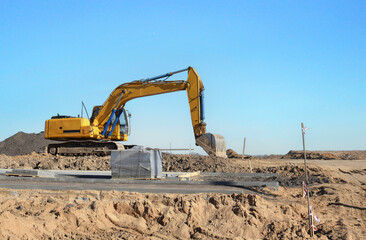 Excavator on earthmoving at construction site. Backhoe digs sand on blue sky background. Construction machinery for excavation, loading, lifting and groundwork on job sites.