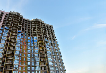 Facade of an unfinished high-rise residential building during construction on blue sky background. Skyscraper and tall house renovation project, government programs.