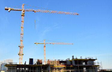Tower cranes working at construction site on blue sky background. Construction process of the new modern residential buildings