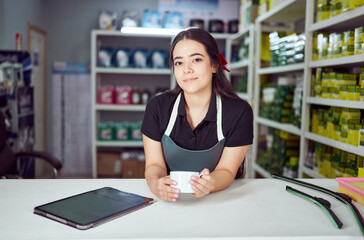 latin american woman salesperson of a small auto parts store holds a cup of coffee
