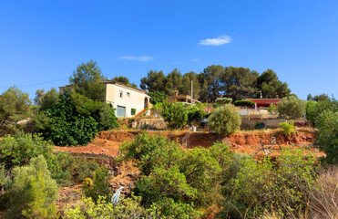 Fototapeta premium Farmhouse in Spanish village. Village with country houses near orange field. Agricultural field at rural houses in mountains. Rural landscape. Villa near farm field. Rural home on hills in countryside