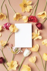 Beautiful aesthetic flowers with empty paper blank on neutral background top view. Minimal...