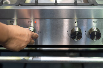 Hand adjusting temperature knob on a modern stainless steel range