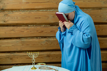 Obraz premium A Jewish woman in a blue veil at the table applies the siddur to her forehead