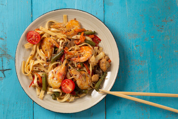 shrimp and udon vegetables pad thai sauce and chopsticks on a blue table. copy space.