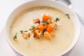 Cream soup in a bowl with croutons and vegetables, garnished with thyme. Top view, close-up. Selected focus.