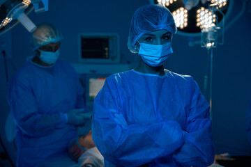 Female doctor in surgical uniforms standing in dark modern operating room