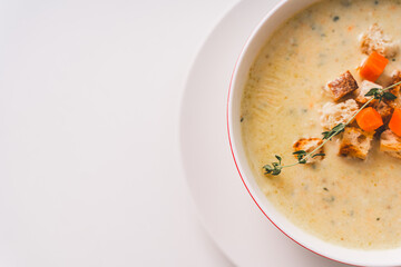 Cream soup in a white bowl with carrots, croutons and thyme on a white table. Copy space. close-up.
