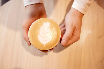 top view of a woman's hands with a cup of frothy latte
