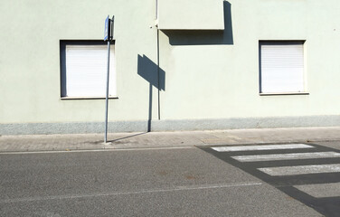 Pedestrian crossing sign on sidewalk with light green facade with white plastic shutter windows on...