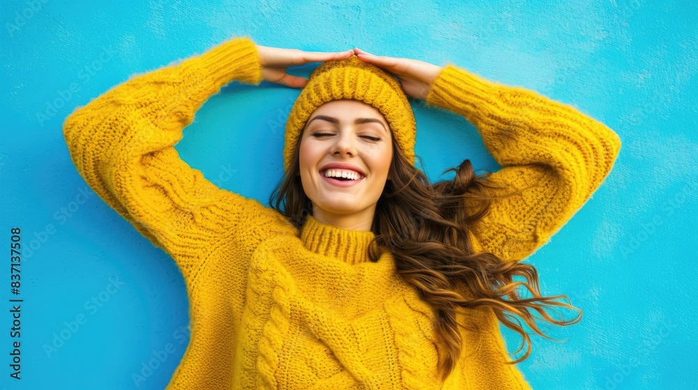 Wall mural A woman in a yellow sweater and hat is smiling and laying on her back. Concept of relaxation and happiness