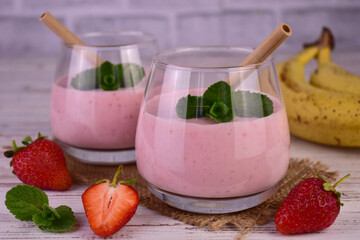 Strawberry banana smoothie in glasses on a white wooden background.
