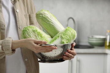 Woman holding fresh chinese cabbages in kitchen, closeup. Space for text