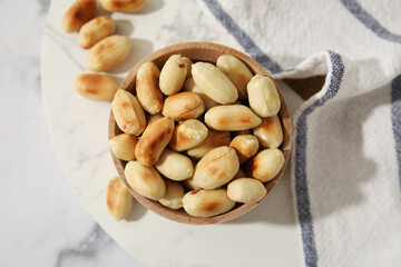 Roasted peanuts in bowl on white marble table, top view