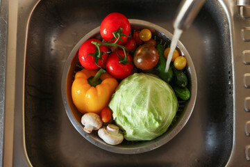 Washing different vegetables with tap water in metal colander inside sink, top view