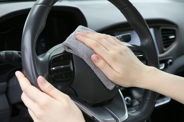 Woman cleaning steering wheel with rag in car, closeup