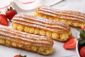 Delicious eclairs filled with cream and strawberries on table, closeup
