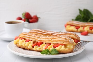 Delicious eclairs filled with cream, strawberries and mint on white table