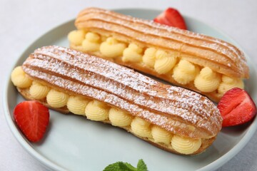 Delicious eclairs filled with cream and strawberries on table, closeup