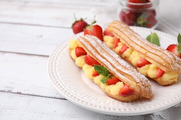 Delicious eclairs filled with cream, strawberries and mint on white wooden table, closeup