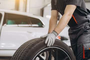 Obraz premium Close-up Car Mechanic holding a tire at the repair garage. Replacement of winter and summer tires