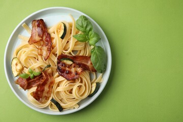 Tasty pasta with bacon and basil on light green table, top view. Space for text