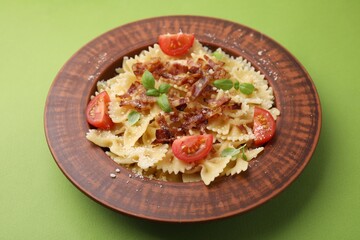 Tasty pasta with bacon, tomatoes and basil on light green table