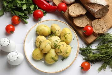 Tasty young boiled potatoes with dill and other products served on white table, flat lay