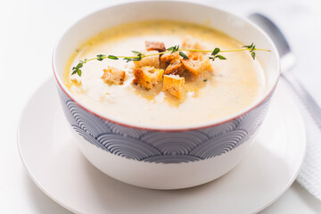 Cream soup with croutons and thyme in a plate on a white table. Selected focus.